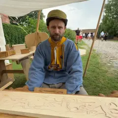 Snycerz co robi? Rzeźbi w drewnie, tworząc misterny wzór na desce.