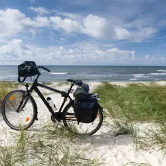 Rower z sakwami na plaży, gotowy do podróży trasą rowerową R10. Morze i niebo w tle.