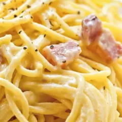 Ein Teller Spaghetti Carbonara, klassisch italienisch zubereitet mit cremiger Sauce und Speckwürfeln, bestreut mit schwarzem Pfeffer.