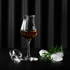 Szklanka Glencairn z bursztynowym trunkiem, obok leży jej zakrętka, lód i rozmaryn. Jak dobrać odpowiednie szkło Glencairn vs tumbler vs copita.