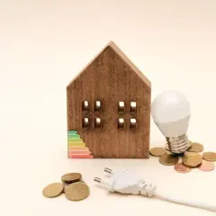 Drewniany domek z etykietą energetyczną, żarówką i monetami. Zastanawiasz się, ile prądu zużywa lampka nocna?