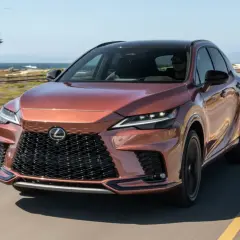 Miedziany Lexus RX 500h jedzie wzdłuż wybrzeża. Słońce odbija się od jego lśniącej karoserii.