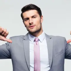 Mężczyzna w garniturze z wybujałym ego pokazuje kciuki w dół, jakby mówił: "Jestem najlepszy, a reszta się myli".
