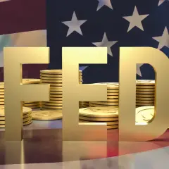 Złote litery "FED" na tle flagi USA i stosów monet. FOMC to komitet, który decyduje o polityce pieniężnej.
