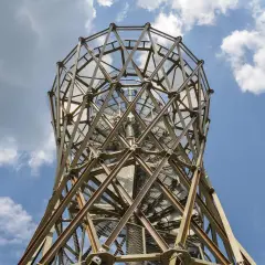 Metalowa konstrukcja wieży widokowej, przypominająca spiralę, wznosi się ku niebu. W oddali widać borowa góra.
