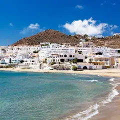 Costa blanca con aguas verde esmeralda, roquetas de mar, y casas blancas en la ladera.