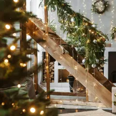 Świąteczne lampki oplatają drewniane schody i choinkę, tworząc magiczny klimat. Zobacz, jak przyczepić lampki do ściany, by uzyskać ten efekt.