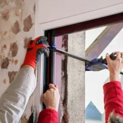 Pose d'une porte d'entrée sur dormant existant. Un ouvrier utilise un serre-joint pour ajuster le cadre.