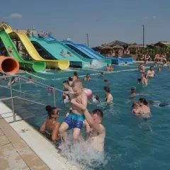 Ludzie kąpią się w basenie z kolorowymi zjeżdżalniami wodnymi w słoneczny dzień.