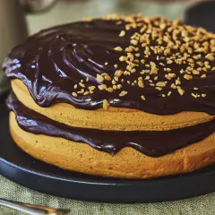 Gâteau sans oeuf à deux étages, nappé de chocolat noir brillant et parsemé de noisettes concassées. Un délice pour tous !