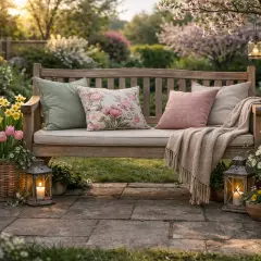 Eine Holzbank im Garten, liebevoll dekoriert mit Kissen, Decke, Blumen und Laternen. Perfekt, um den Frühling zu genießen.
