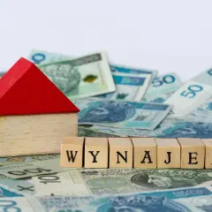 Drewniany domek i kostki z napisem "WYNAJEM" na tle polskich banknotów. Zgłoszenie umowy najmu do urzędu skarbowego.