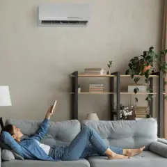 Mujer relajada en el sofá, usando el control remoto para programar el aire acondicionado y disfrutar de la temperatura perfecta.