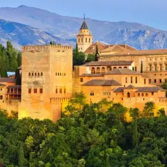 Alhambra, jeden z najpiękniejszych zabytków w hiszpańskich miastach, wznosi się na wzgórzu otoczony zielenią, z górami w tle.