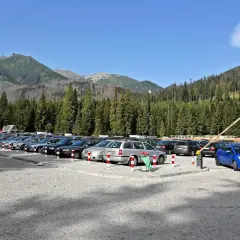 Parking Morskie Oko, cena za postój. Rząd samochodów na kamienistym parkingu, w tle las i góry.