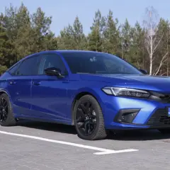 Błękitny Honda Civic 11. generacji z czarnymi felgami zaparkowany na tle lasu.