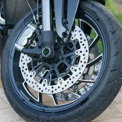 Rueda de moto con disco de freno perforado y pinza. Parece que hay un pinchazo lateral en la rueda, listo para ser reparado.