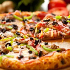 Pyszna pizza z gotowego ciasta, obficie posypana serem, oliwkami, papryką i mięsem. Ser ciągnie się apetycznie.