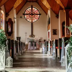 Piękna dekoracja kościoła na ślub samemu: ławki ozdobione zielenią i lampionami, ołtarz z kwiatami.