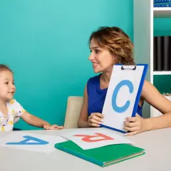 Nauczycielka pokazuje dziecku literę C, ucząc je, jak nauczyć dziecko głoskowania. Na stole litery A i R.