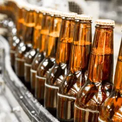 Szklane butelki piwa bezalkoholowego na linii produkcyjnej. Czy piwo bezalkoholowe jest zdrowe? To pytanie nurtuje wielu konsumentów.