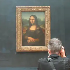 Ein Mann fotografiert die Mona Lisa. Die Frage, wie lange hat Da Vinci für die Mona Lisa gebraucht, beschäftigt viele Besucher.