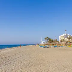 Amplia playa de la urbanización de Roquetas con sombrillas, tumbonas y edificios hoteleros al fondo.