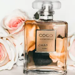 Szklana butelka perfum Chanel Coco Mademoiselle otoczona jasnoróżowymi różami.