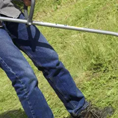 Osoba w dżinsach i koszuli używa podkaszarki do trawy, kiedy pierwsze koszenie trawy po zasianiu.