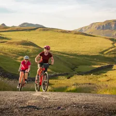 Two women enjoy a scenic ride on their bikes through rolling green hills, a perfect example of England bike tours.