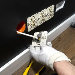 Instalacja gniazdek elektrycznych. Ręka w białej rękawiczce podłącza przewód do mechanizmu gniazdka. W ścianie widać już kilka zamontowanych gniazdek. Zastanawiasz się, ile za punkt elektryczny?