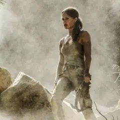 Alicia Vikander jako Lara Croft, wspinająca się po skalistym terenie, otoczona pyłem i mgłą.