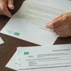 Dłonie przeglądają dokumenty ZUS. Informacje o świadczeniach i tym, jak przejść na emeryturę, są kluczowe.