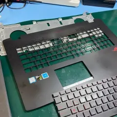 Części laptopa ROG gotowe do wymiany klawiatury. Widoczna górna obudowa z miejscem na klawisze i nowa klawiatura z czerwonymi oznaczeniami.