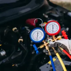 Serwis klimatyzacji samochodowej cennik: mechanik z manometrami sprawdza układ chłodzenia auta.