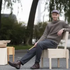 Erik Eje Almqvist sitter på en trästol med en hammare i handen, omgiven av trämaterial.