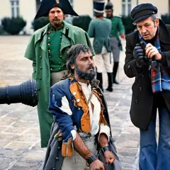 Scena z planu filmowego w polska lat 80. Uwięziony mężczyzna w zniszczonym stroju, obok żołnierze i reżyser.