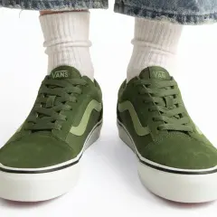 Zielone buty Vans na białym tle, widoczne od przodu, z nogawkami w białych skarpetkach i dżinsach.