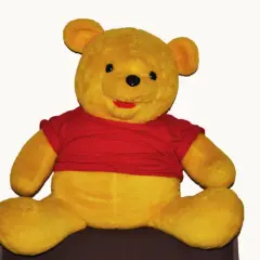 Pluszowy Kubuś Puchatek w czerwonej koszulce siedzi na ciemnym tle.