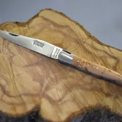 Navaja Laguiole artesanal, con mango de madera veteada y detalles plateados, reposa sobre un tocón de árbol.