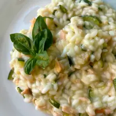 Un cremoso risotto con verdure, zucchine e pezzetti di salmone, guarnito con foglie di basilico fresco.