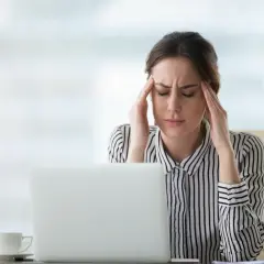 Kobieta z bólem głowy przy laptopie, zastanawia się, ketoza co to.