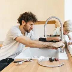 Padre e figlio installano un nuovo rubinetto in cucina, un'operazione delicata per spostare attacchi cucina senza rompere pavimento.
