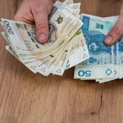 Ręce trzymają stos banknotów 50 i 200 zł. Marzenie o samochodzie elektrycznym limit kosztów staje się realne.