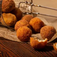 Croquetas de patata y pollo doradas y crujientes, algunas en una cesta metálica, otras sobre papel de estraza.