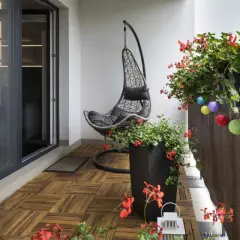 Un balcone accogliente con pavimento in legno, una sedia sospesa e fiori rossi. Un'idea per rivestire pavimento balcone fai da te.