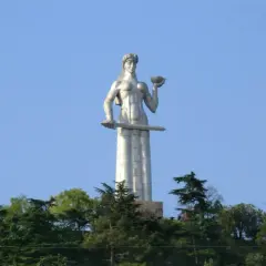 Matka Gruzja, symbol Tbilisi, trzyma miecz i puchar. Monumentalna postać wznosi się nad zielenią.