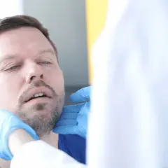 Lekarz bada gardło pacjenta, który skarży się na chrzakanie u dorosłego.