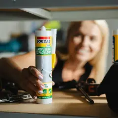 Kobieta trzyma tubkę akrylu, zastanawiając się, ile schnie akryl. Na stole leżą narzędzia.