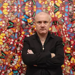 Damien Hirst stoi przed ścianą ozdobioną jego dziełami z motyli.
